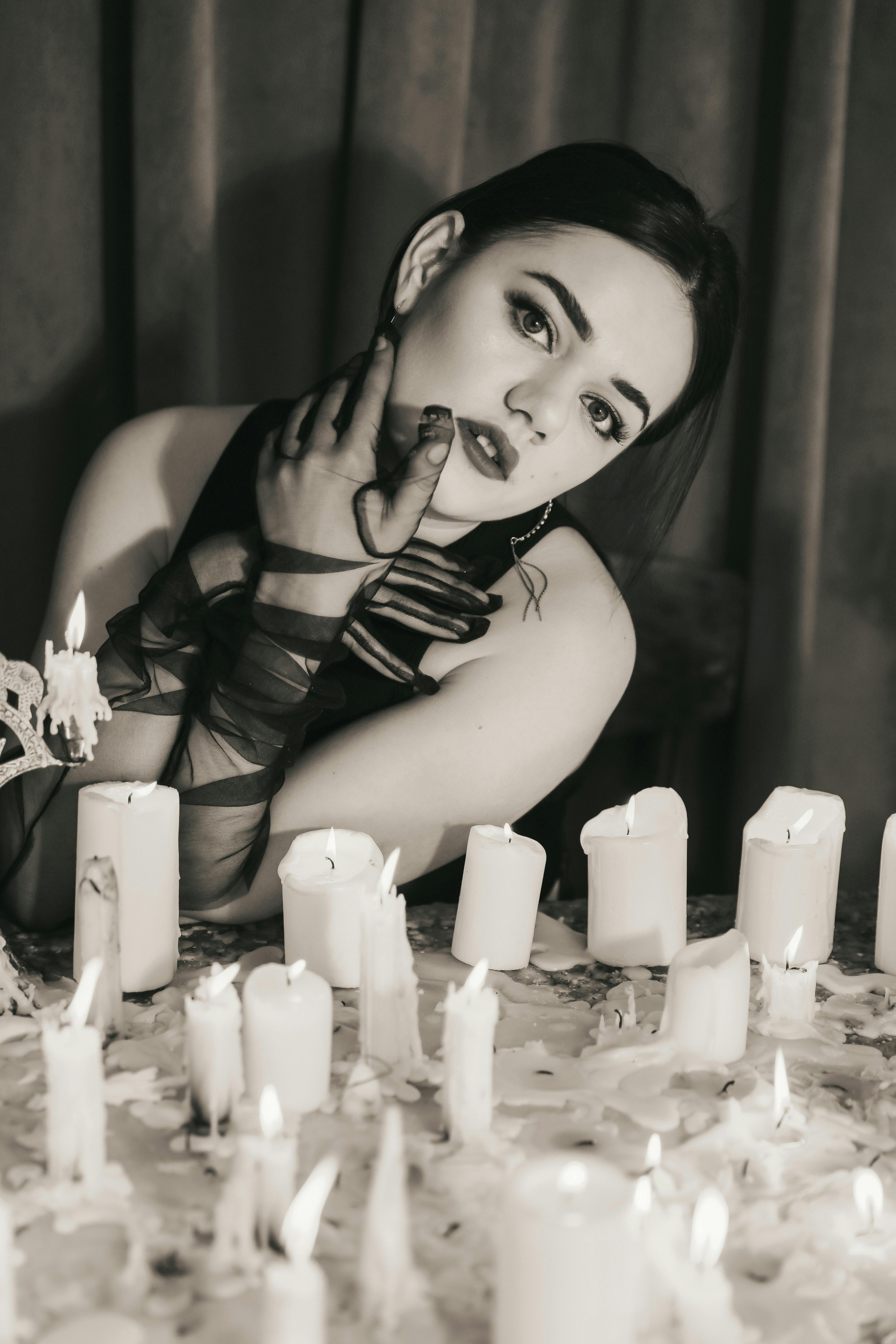 Free A dramatic portrait of a woman in a dimly lit setting surrounded by burning candles, exuding a mysterious vibe. Stock Photo