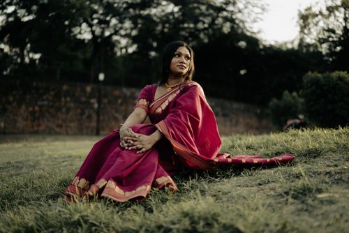 Free Indian woman in traditional pink sari sitting outdoors at sunset, exuding elegance. Stock Photo
