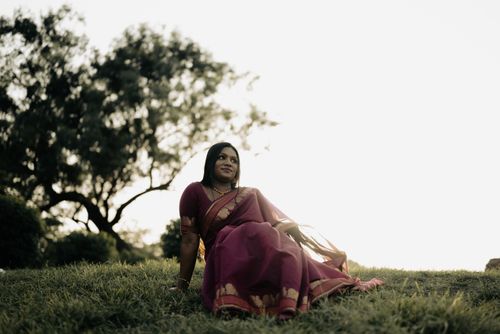 Free A South Asian woman in a vibrant sari sits happily in a scenic outdoor setting, embracing cultural elegance. Stock Photo