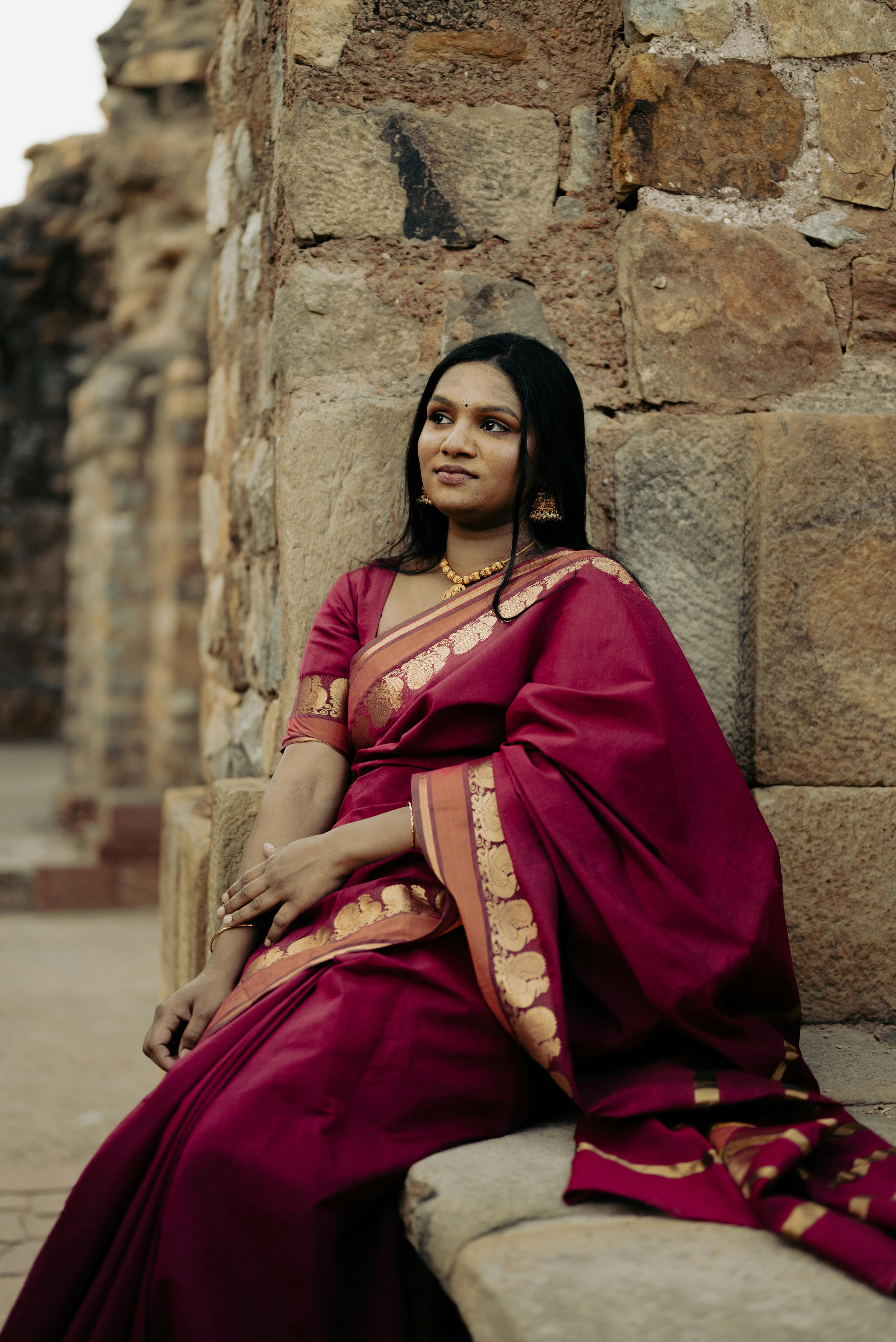 身穿传统红色纱丽的女子在古老的石墙上优雅地摆姿势，体现了优雅和文化服饰