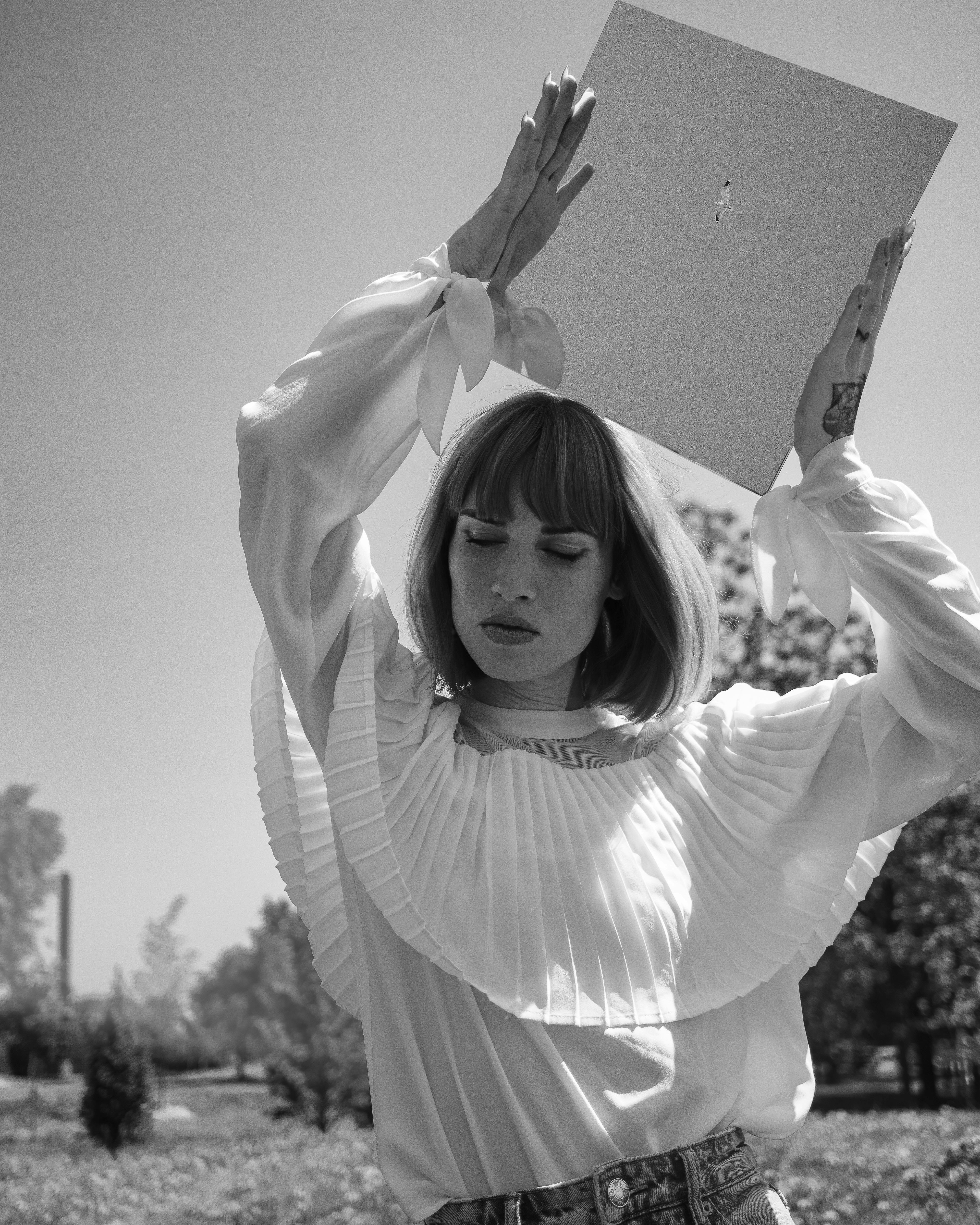 A stylish woman with a bob haircut poses elegantly outdoors holding a board.