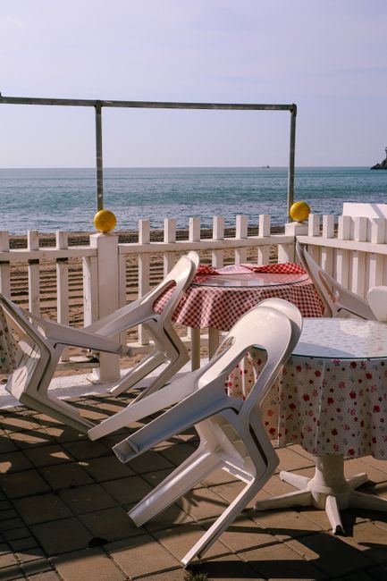 Plastic chairs and tables along a beachfront with ocean view, perfect for a tranquil vacation spot.