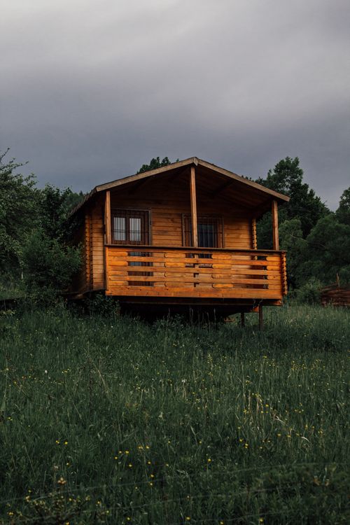 Free Charming wooden cabin surrounded by green meadows under cloudy sky. Stock Photo
