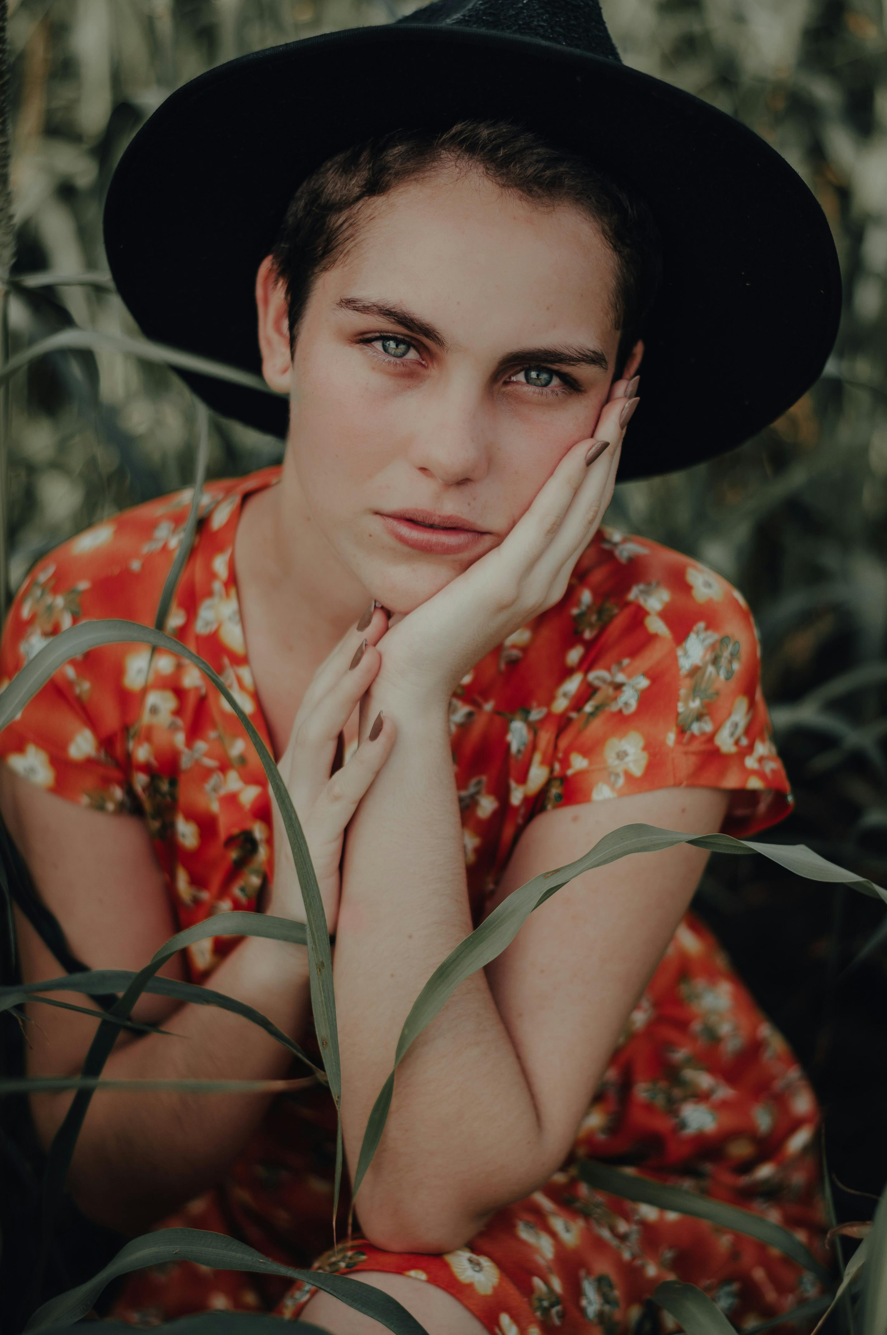 Artistic close-up portrait of a woman in a floral dress and hat outdoors.