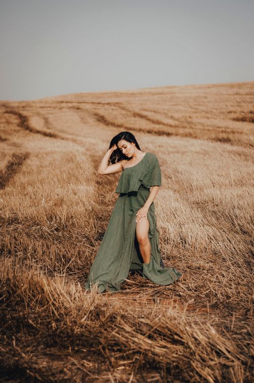 Free A woman in a flowing green dress poses gracefully in a sunlit golden field. Stock Photo
