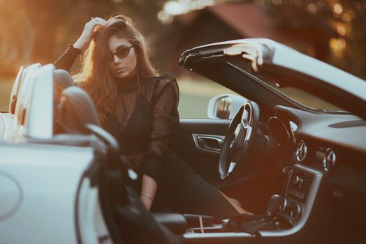 Woman in sunglasses sitting in a convertible during golden sunset.