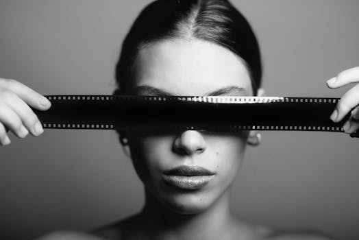 Conceptual black and white portrait of a woman with a film strip covering her eyes.
