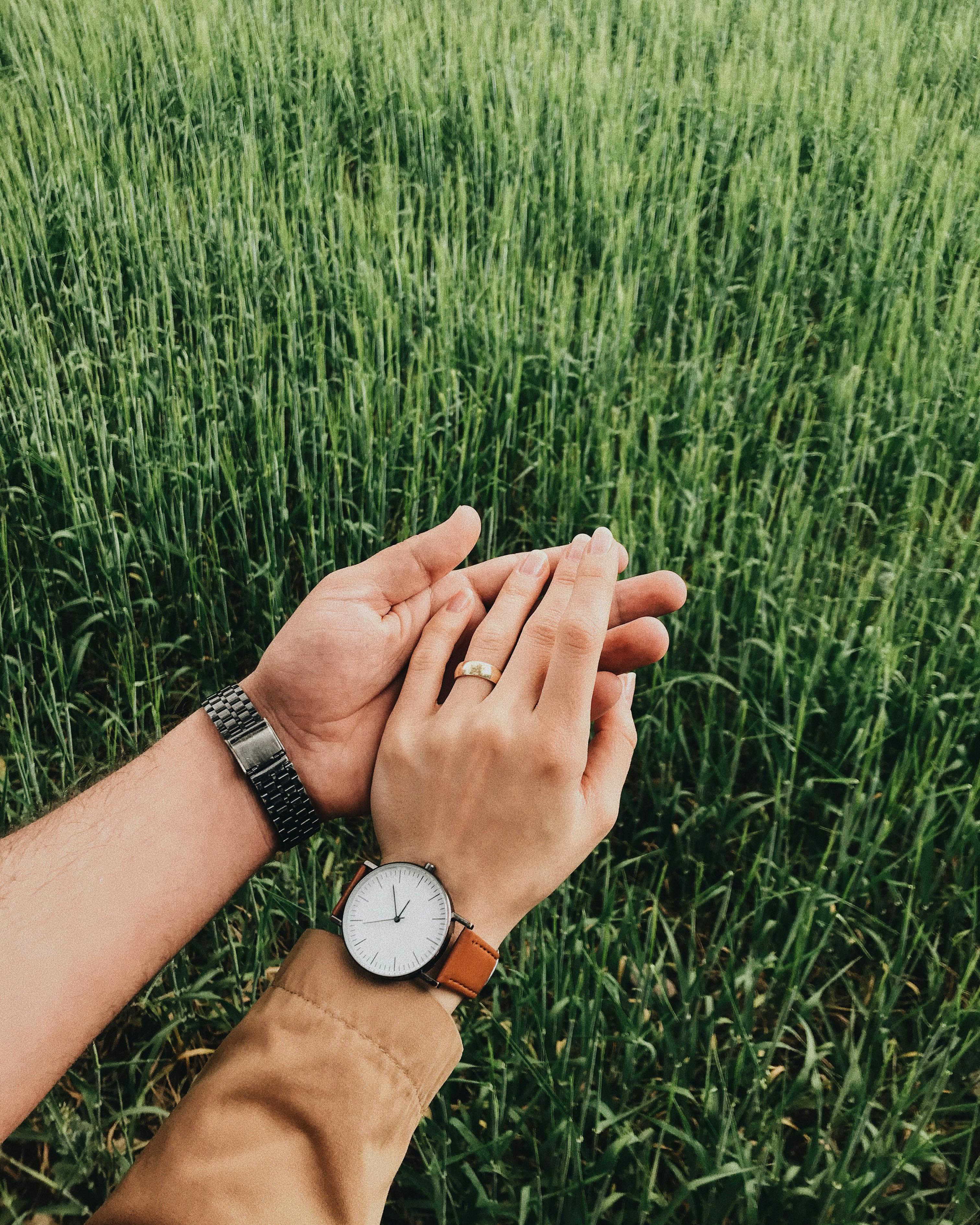 A romantic moment as a couple holds hands with watches in a green field.