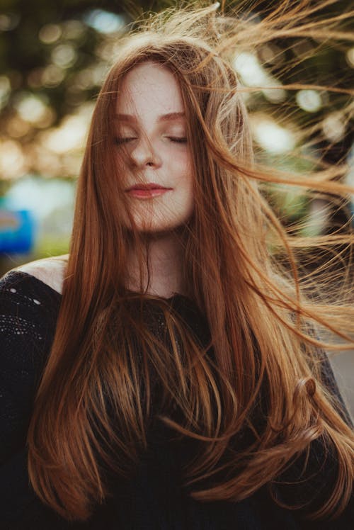 Free Young Redhead Standing Outdoors with Her Hair Messed by the Wind  Stock Photo