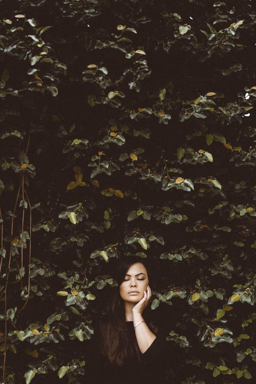 Free A young woman stands serenely with closed eyes against a vibrant green hedge. Stock Photo