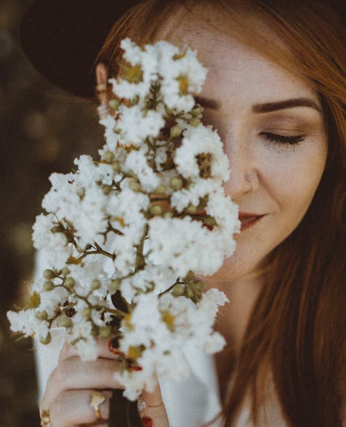 Young Redhead Holding a Branch with White Flowers next to Her Face