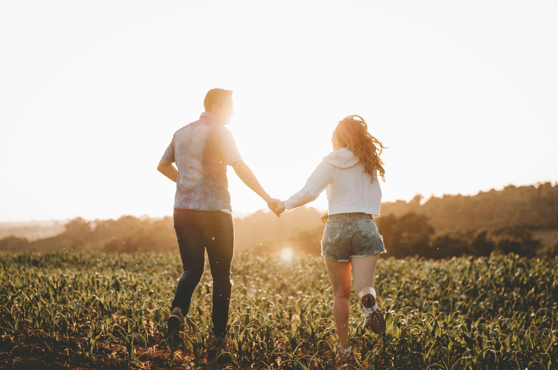 A couple joyfully running hand in hand through a sunlit field