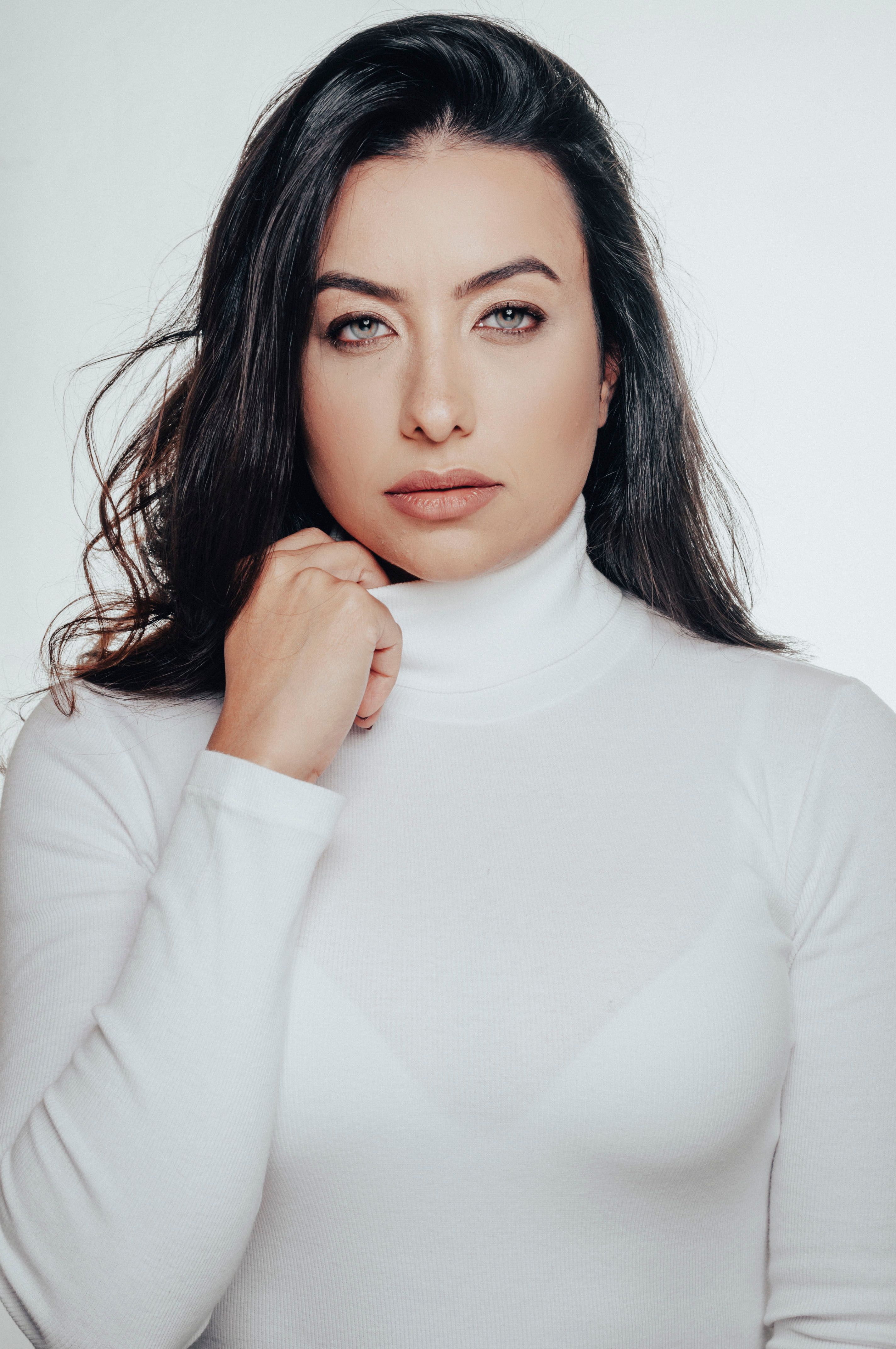 Studio portrait of a young woman with long hair in a white turtleneck, exuding elegance and simplicity.