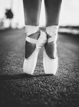 Black and white photo of a ballerina on pointe shoes standing gracefully on a road.