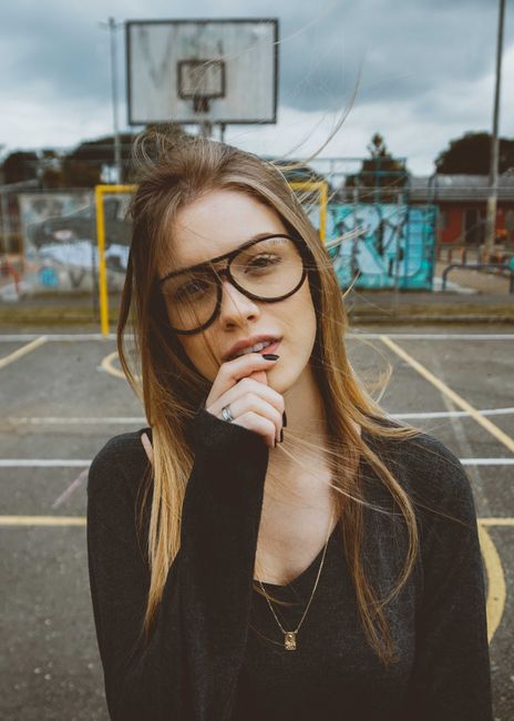 A fashionable young woman with eyeglasses poses confidently on an outdoor basketball court.
