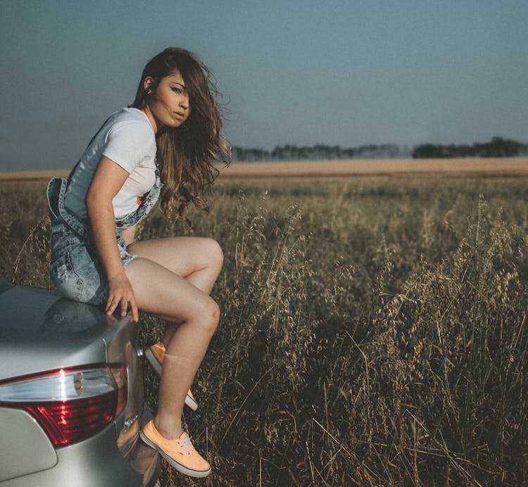 A Girl Sitting On A Car Trunk In The Countryside 