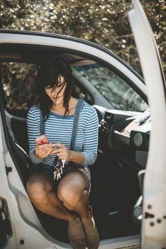 A young woman sitting in a car using her smartphone, enjoying a leisurely road trip on a sunny day.