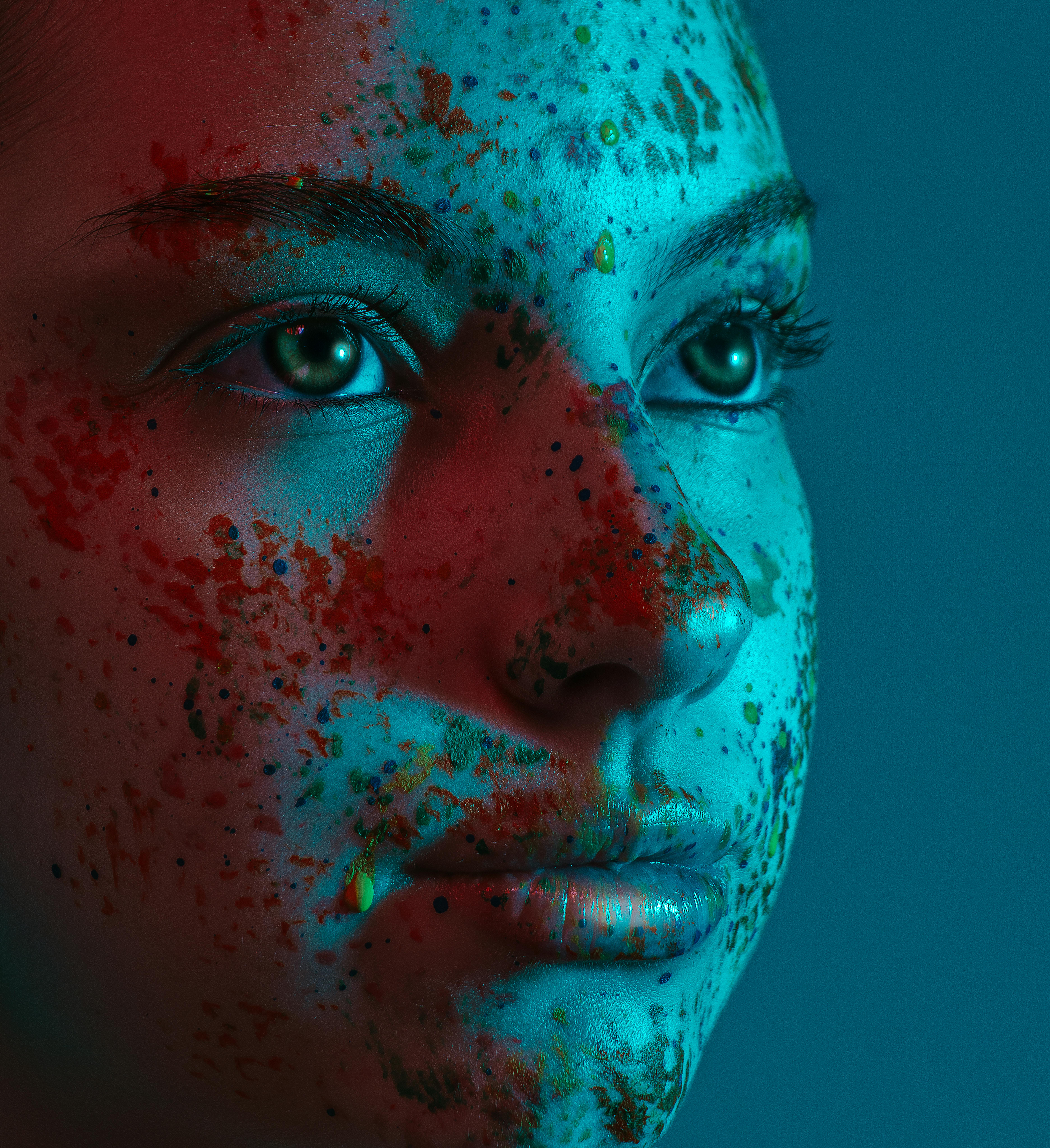 Close-up portrait of a woman with vibrant face paint under dramatic lighting.