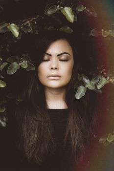 A serene portrait of a woman surrounded by leaves, eyes closed, conveying tranquility and connection with nature.