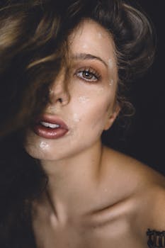 Close-up portrait of a woman with glossy makeup and captivating gaze, accentuating skin texture.