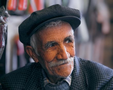 Close-up portrait of a senior man with a mustache and newsboy cap, showcasing his expressive wrinkles.