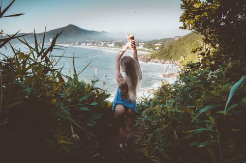 Free A woman embraces summer bliss with a stunning view of the ocean, surrounded by lush greenery. Stock Photo
