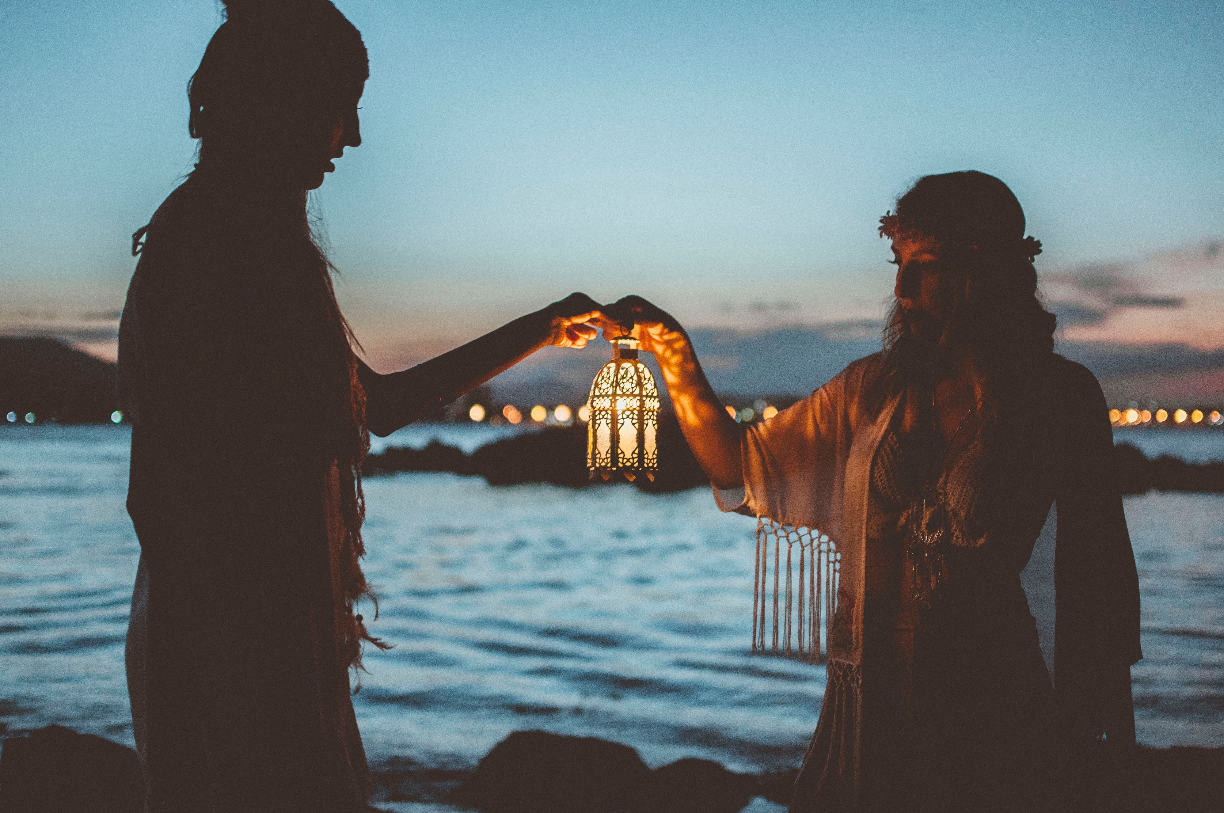 Women Holding Illuminated Lantern at Dawn by Sea · Free Stock Photo
