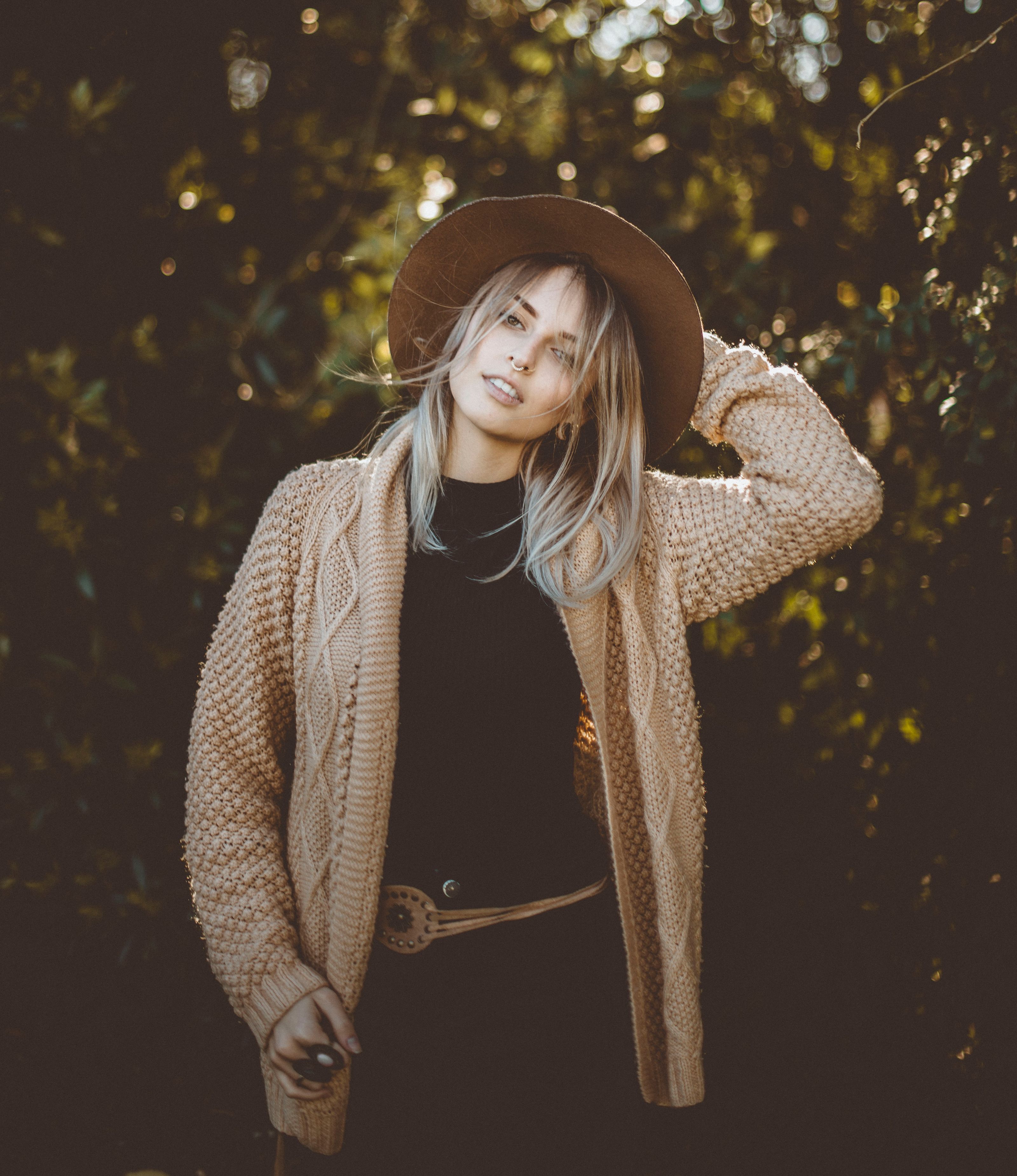 Mulher fashionista em um cardigã aconchegante e chapéu aproveitando um dia ensolarado ao ar livre.