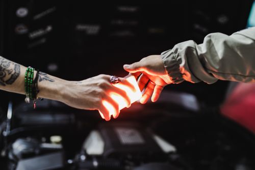 Free A moment of connection captured as two hands pass a glowing light amidst shadows. Stock Photo