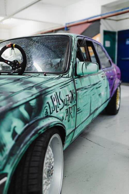 Free A detailed side view of a vibrant vintage car with custom graffiti, showcased in a workshop. Stock Photo