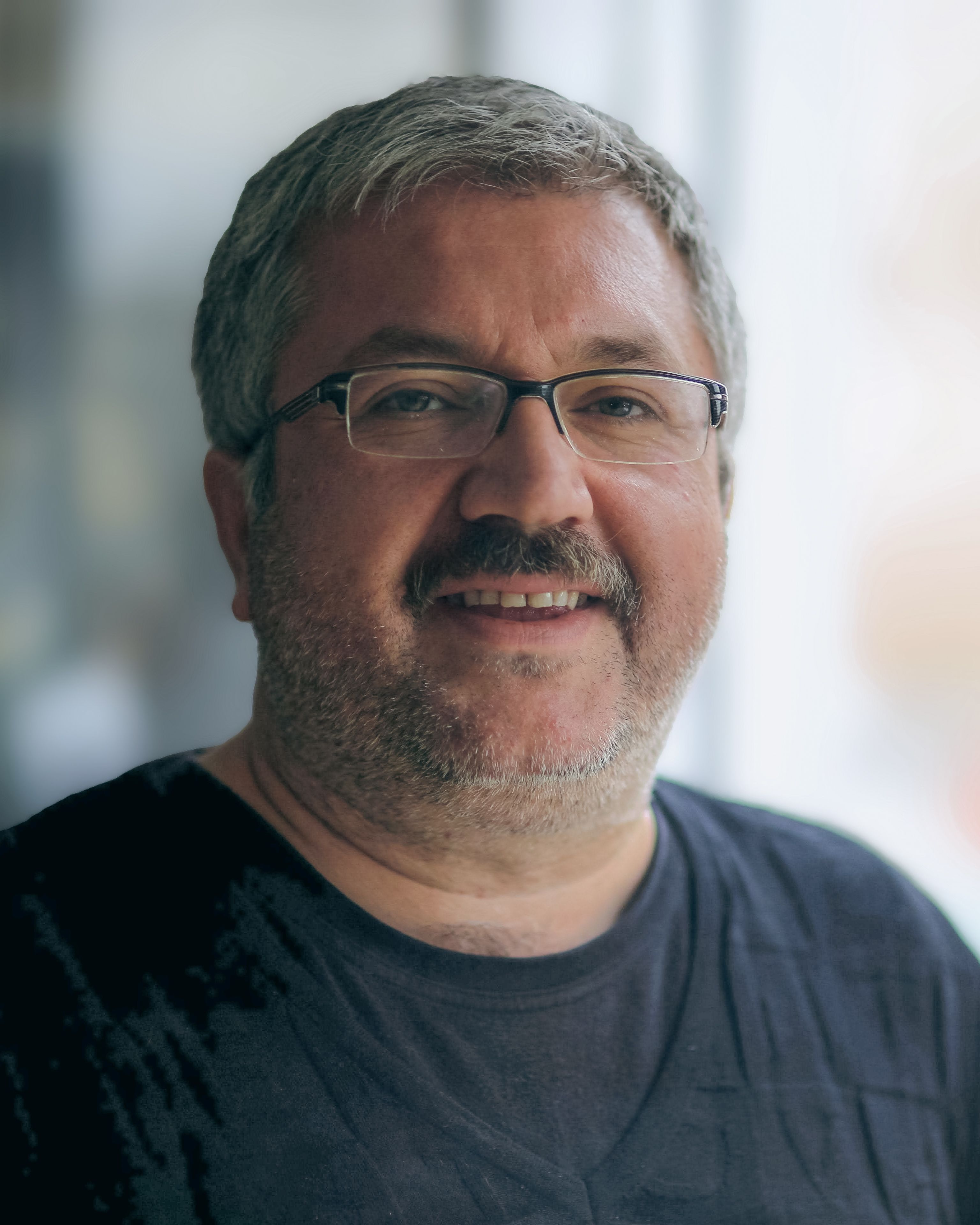 Portrait of a smiling mature man with eyeglasses indoors, gray hair and relaxed demeanor.