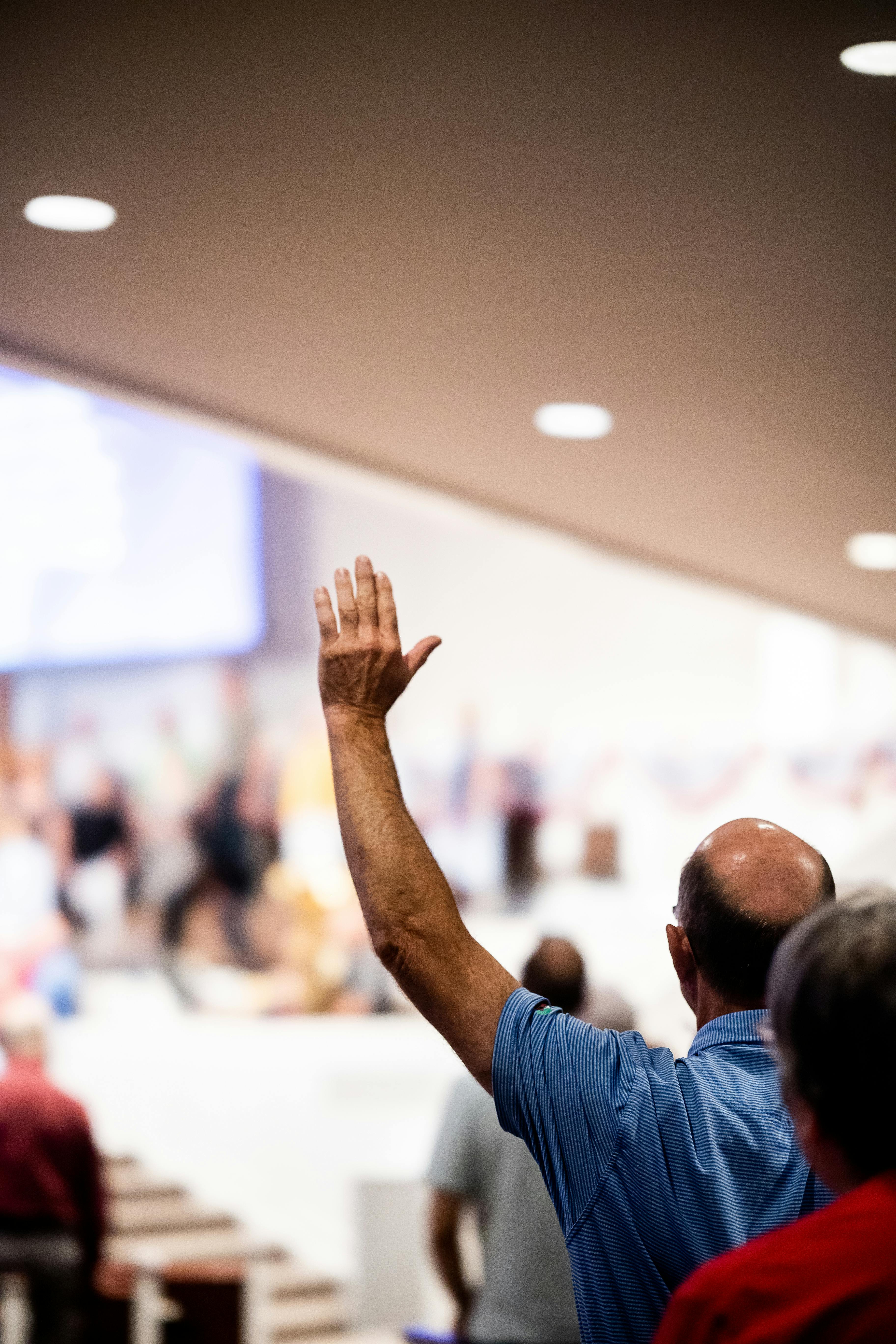 An individual raising a hand during a conference in a modern indoor setting.