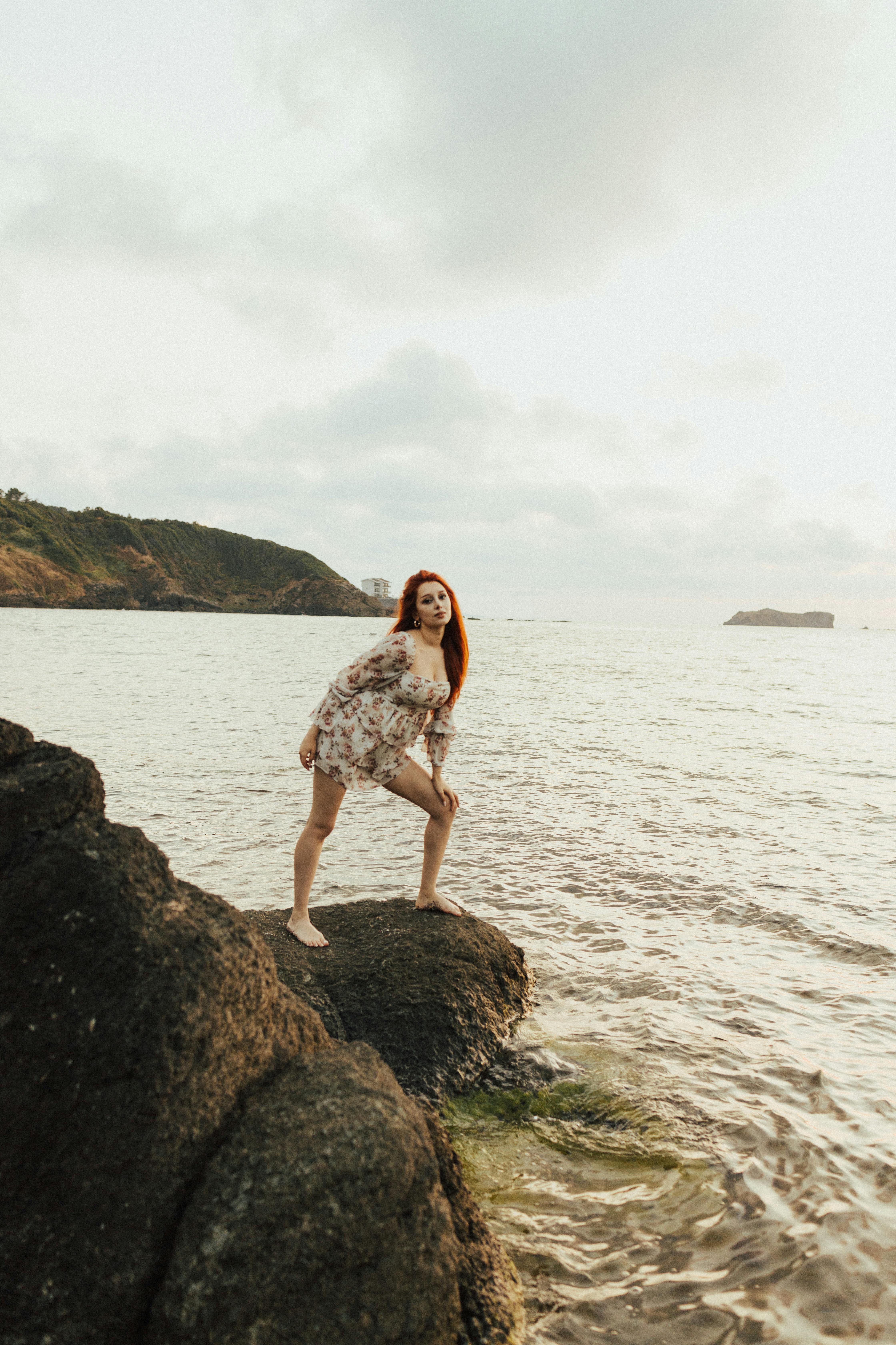 a woman in a dress standing on rocks in the ocean