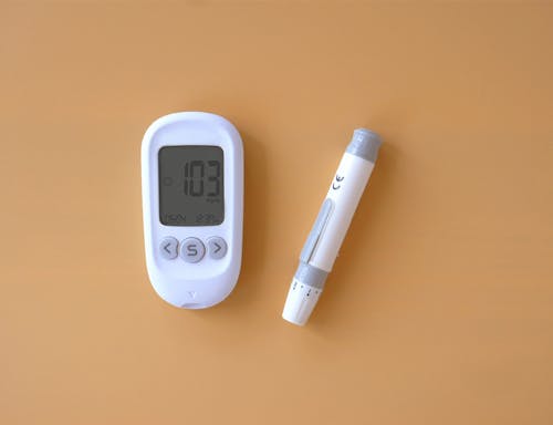 A blood glucose meter and a pen on a yellow background