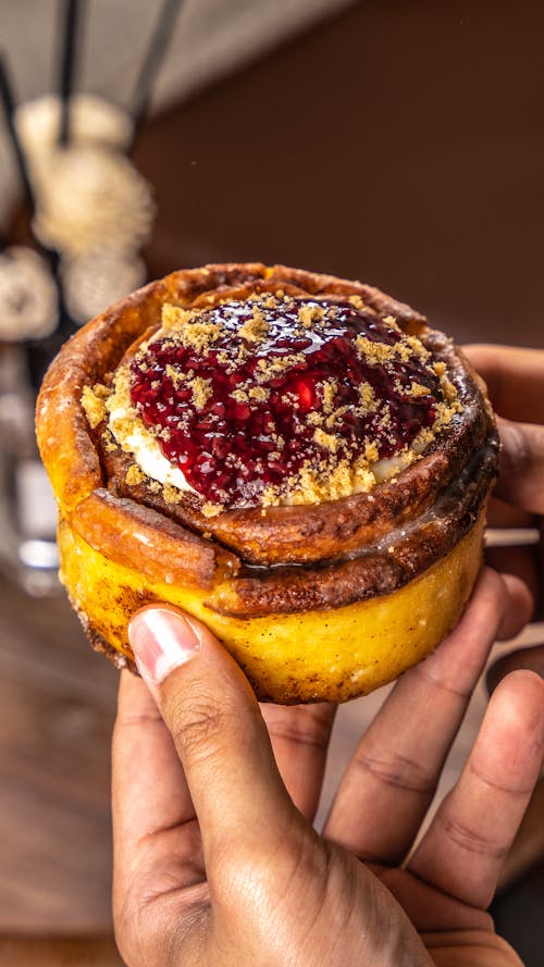 Closeup of a Hand Holding a Swirl Cake with Red Jam