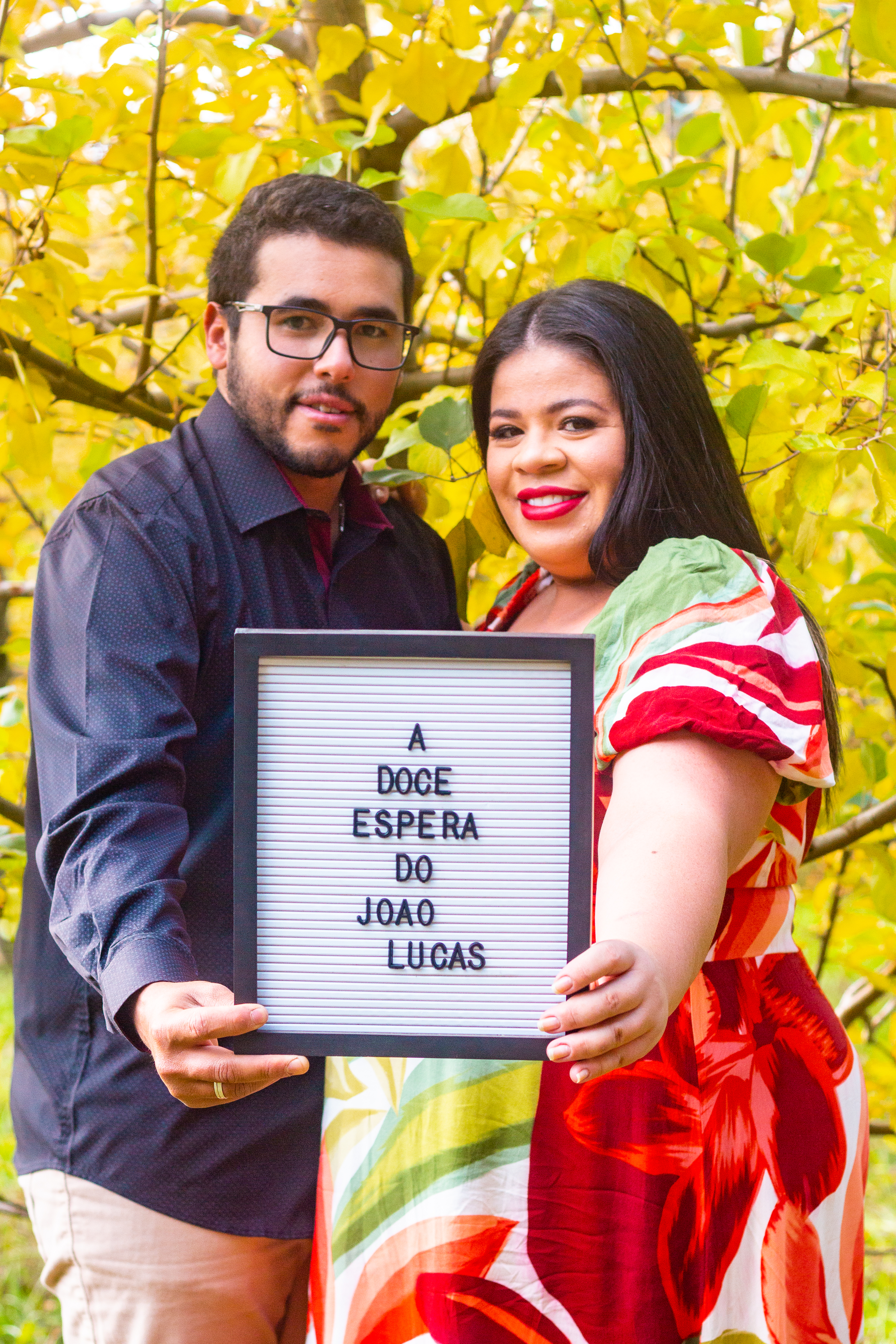 A joyful couple sharing the excitement of pregnancy with a framed message outdoors.