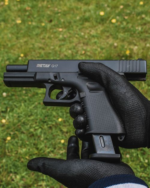 Free Close-up of a gloved person holding a firearm outdoors on grass. Stock Photo