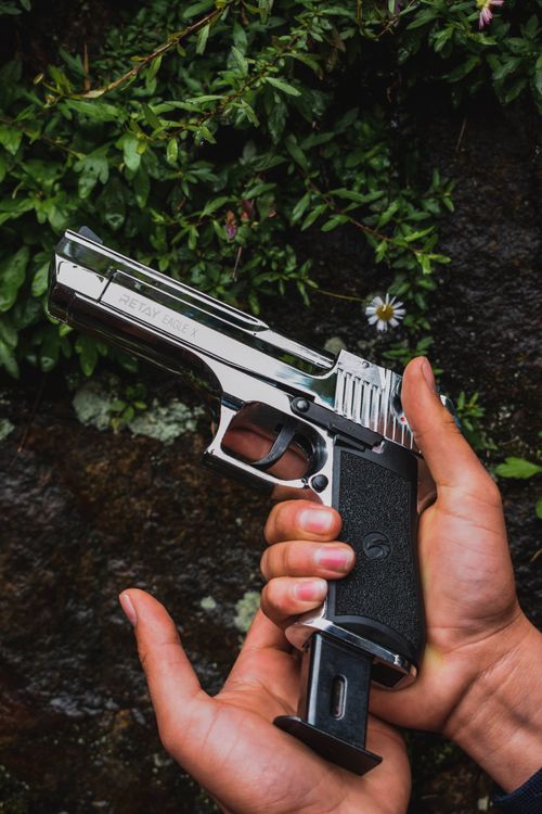 Free Detailed view of hands holding a silver pistol outdoors against a green background. Stock Photo