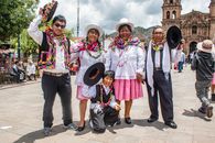 Group of people in traditional clothing celebrating in a historic plaza with a church backdrop.