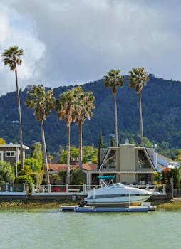 A tranquil harbor scene with a luxury yacht moored in front of palm trees and mountains.