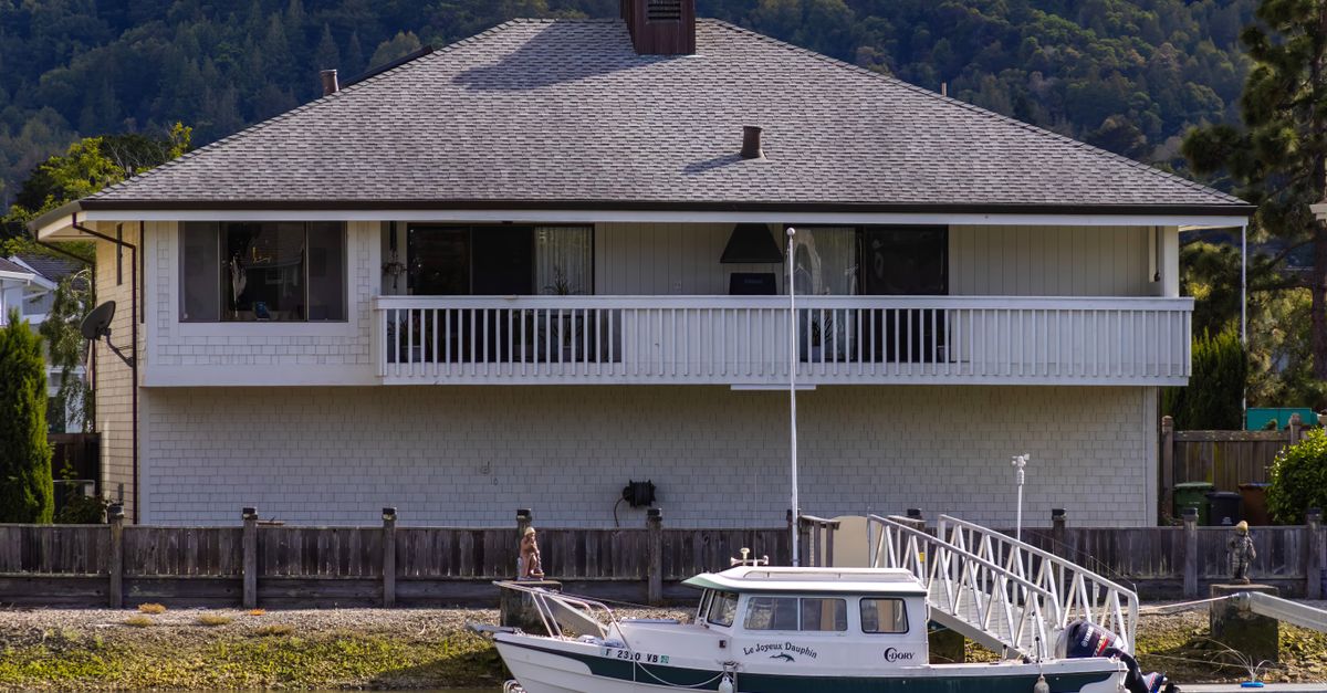 A serene waterfront house with a docked boat in a lush, forested area.