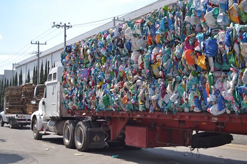 A Truck Loaded with Plastic Trash Driving on a Street in City 