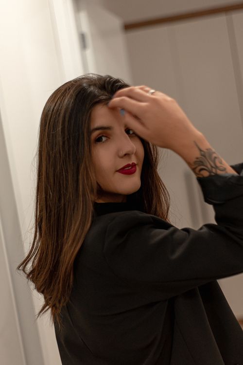 Free Fashionable young woman with tattoos posing indoors, hand in hair, showcasing red lips. Stock Photo