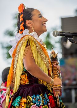 Woman in traditional costume performing on stage with microphone, exuding joy and cultural pride.
