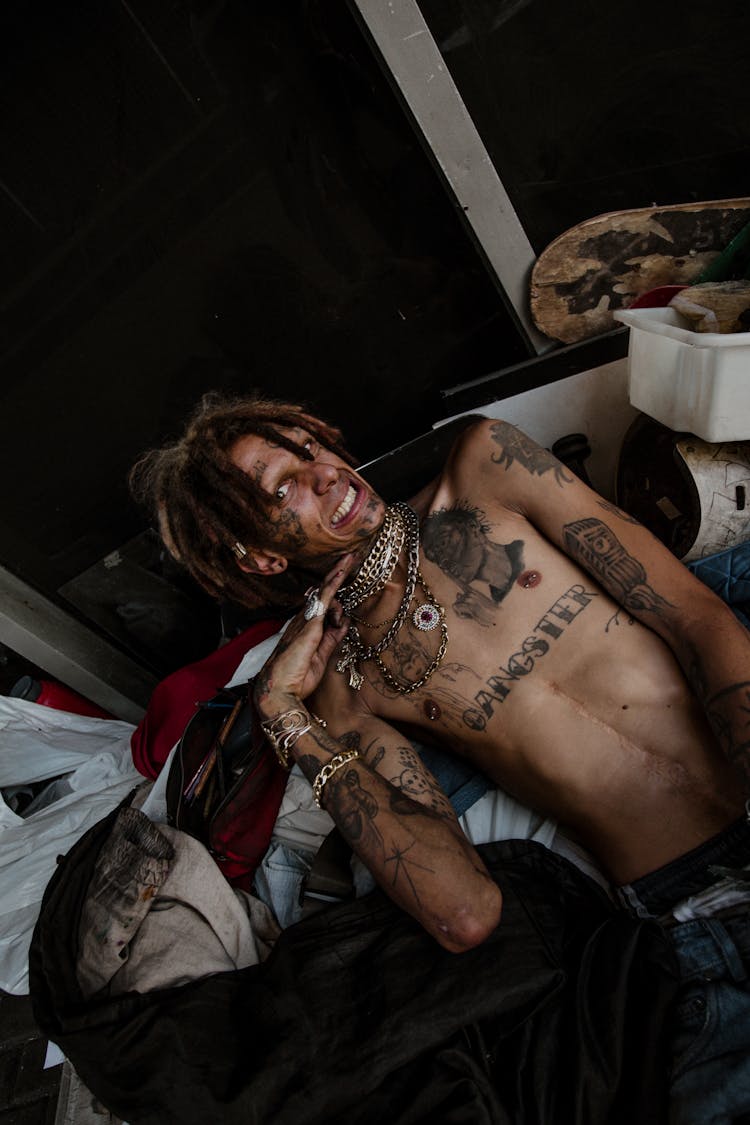 A Shirtless Man With Tattoos Lying On A Pile Of Trash 