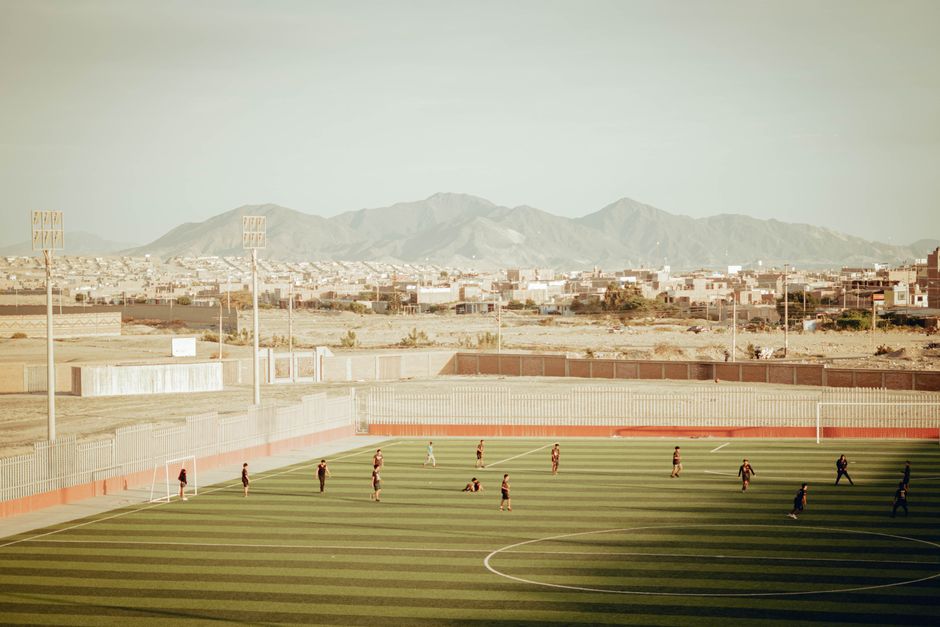 Aerial view of a soccer field with players in Nuevo Chimbote, Peru, against a mountain backdrop.