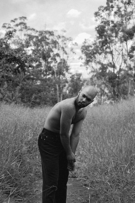 Black and white portrait of a shirtless man standing in grass, Belo Horizonte.