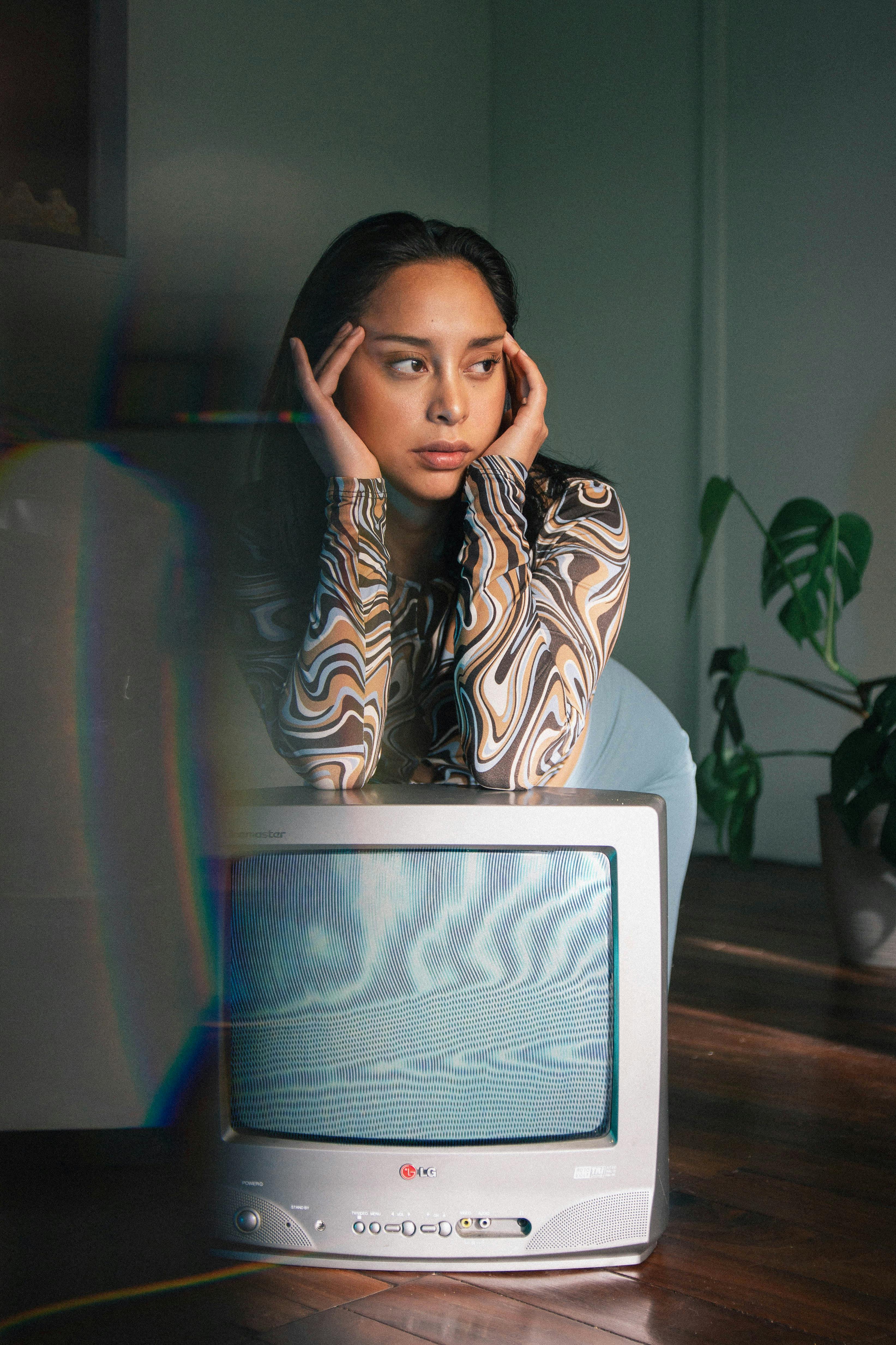 A woman leans on a retro television set, deep in thought, with warm indoor lighting.