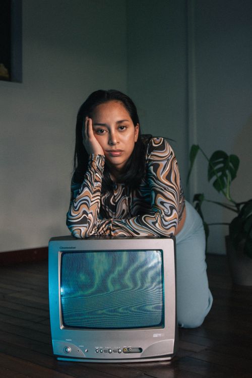 Free A woman kneeling and leaning on a vintage television set indoors, appearing thoughtful. Stock Photo