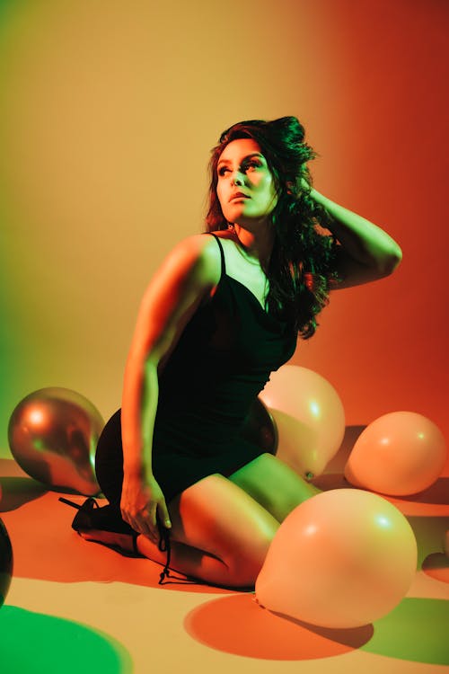 Beautiful Woman in a Black Dress Kneeling with Balloons Lying around her 